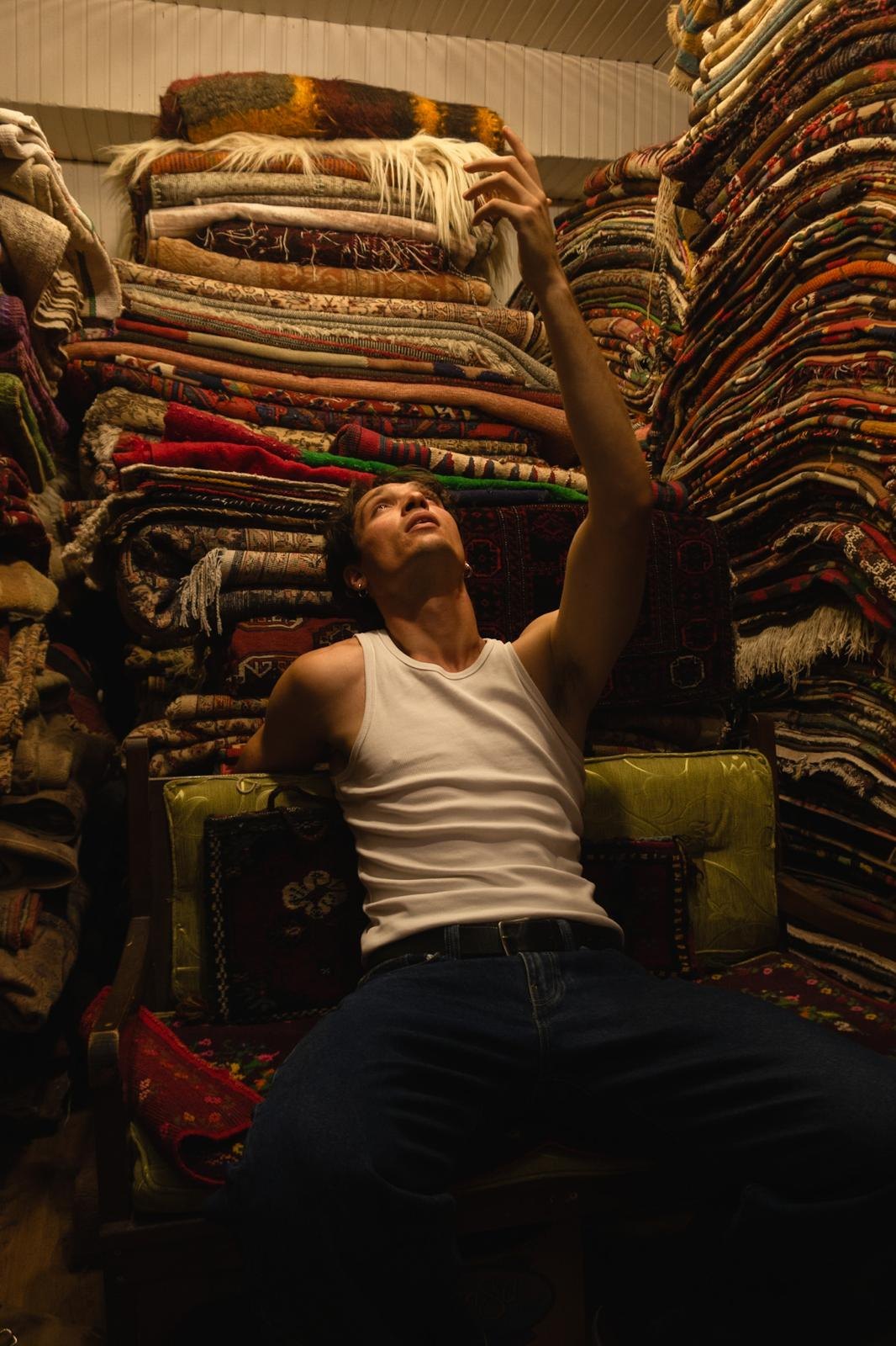 Reaching toward a towering stack of folded antique rugs